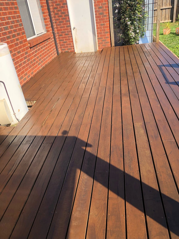 Stained timber deck along the side of a red brick house