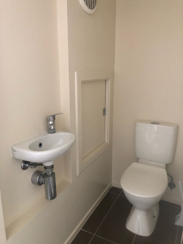Small toilet room with a corner hand basin and cream walls
