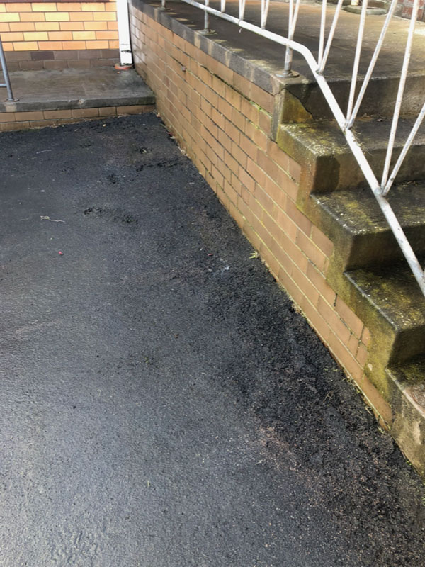 Clean dark asphalt path beside a brick retaining wall and steps