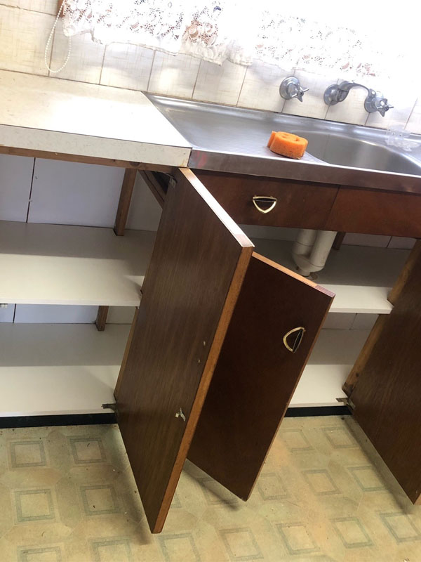 Timber kitchen cupboard doors open under a stainless steel sink